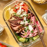 Fully prepared mediterranean steak bowls sit on a yellow tiled surface.