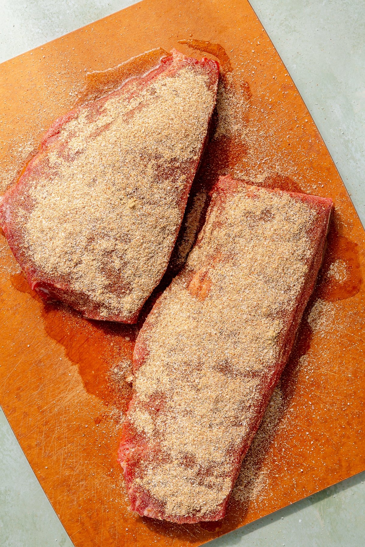 Fully seasoned steaks sit on an orange cutting board.