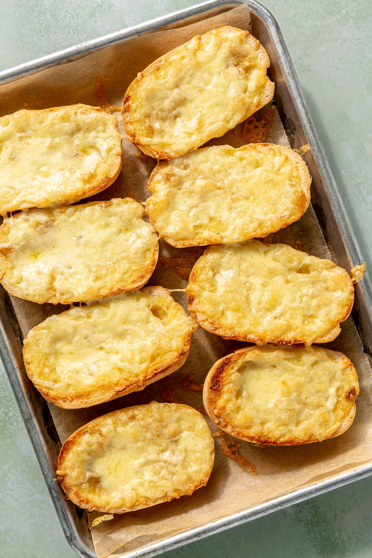 Now toasted, the cheese covered baguette halves sit on a metal baking sheet.