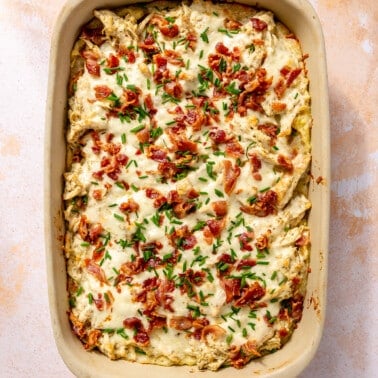 Fully cooked bacon ranch casserole sits in its baking dish on a light pink background. It has been topped with fresh chives.
