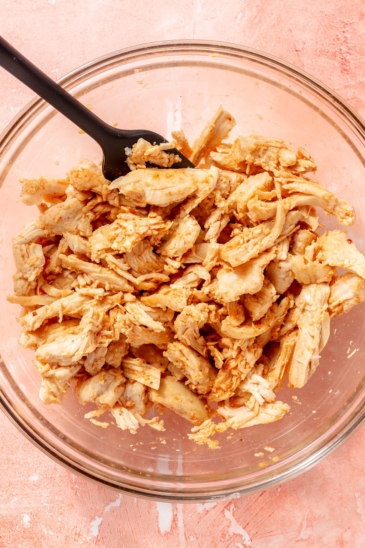 Shredded, seasoned chicken sits in a glass mixing bowl.