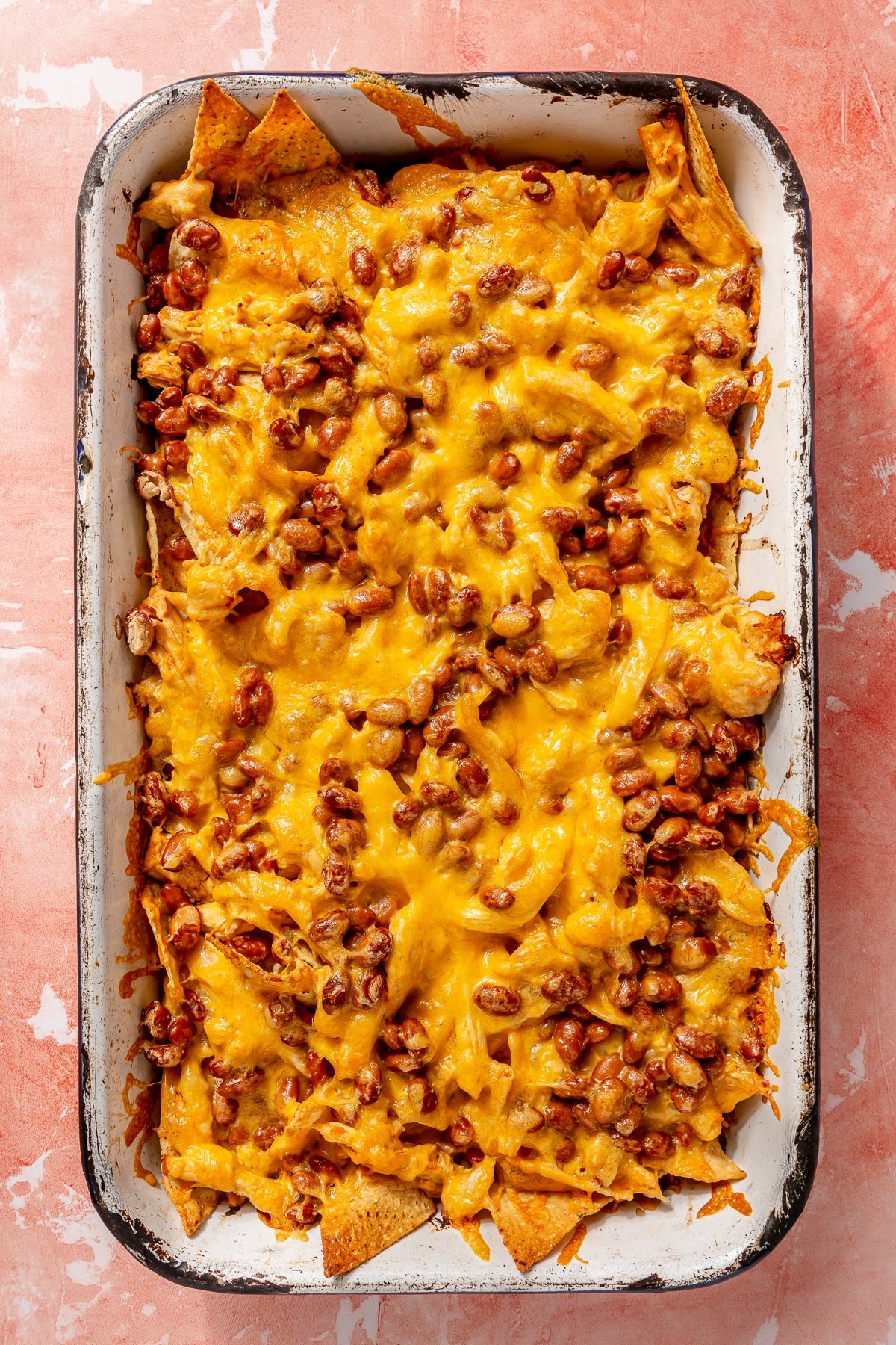 Fully baked sheet pan nachos sit on a white sheet pan.