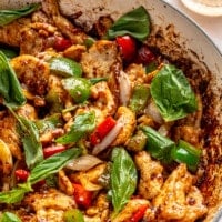 Black pepper chicken stir fry sits in a white pan. Fresh basil has been sprinkled over the top.