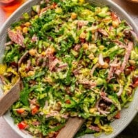 Italian chopped salad sits in a large mixing bowl. A large serving spoon sits to the side.