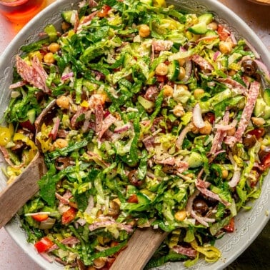 Italian chopped salad sits in a large mixing bowl. A large serving spoon sits to the side.