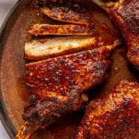 Three cooked and glazed pork chops sit on a brown colored plate. One has been sliced to show the inside.