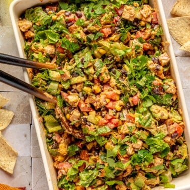 Southwest chopped salad sits in a white rectangular serving dish. A pair of large serving spoons sit to the side.