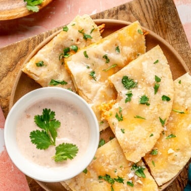 Quartered chicken and cheese quesadillas sit on a brown plate. a light pink colored sauce sits to the side.