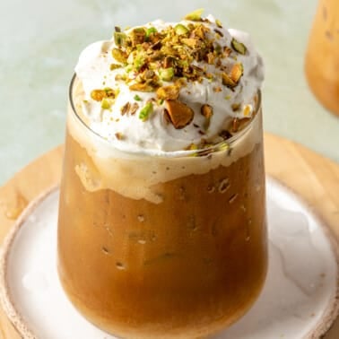 A glass of cold brew with pistachio creamer sits on a wooden plate.