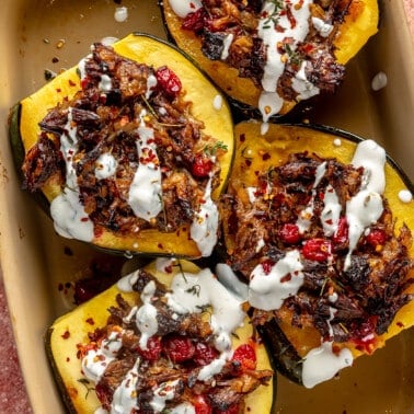 Fully prepared stuffed acorn squash sit in a brown baking dish.