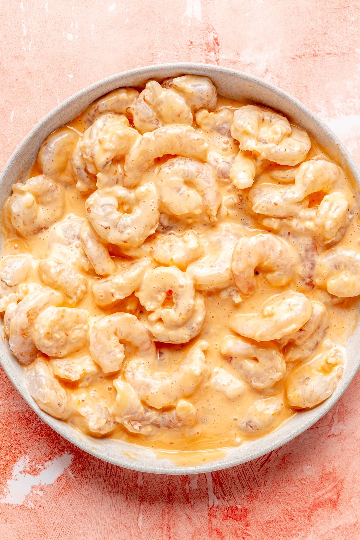 Raw shrimp covered in bang bang sauce in a shallow bowl.