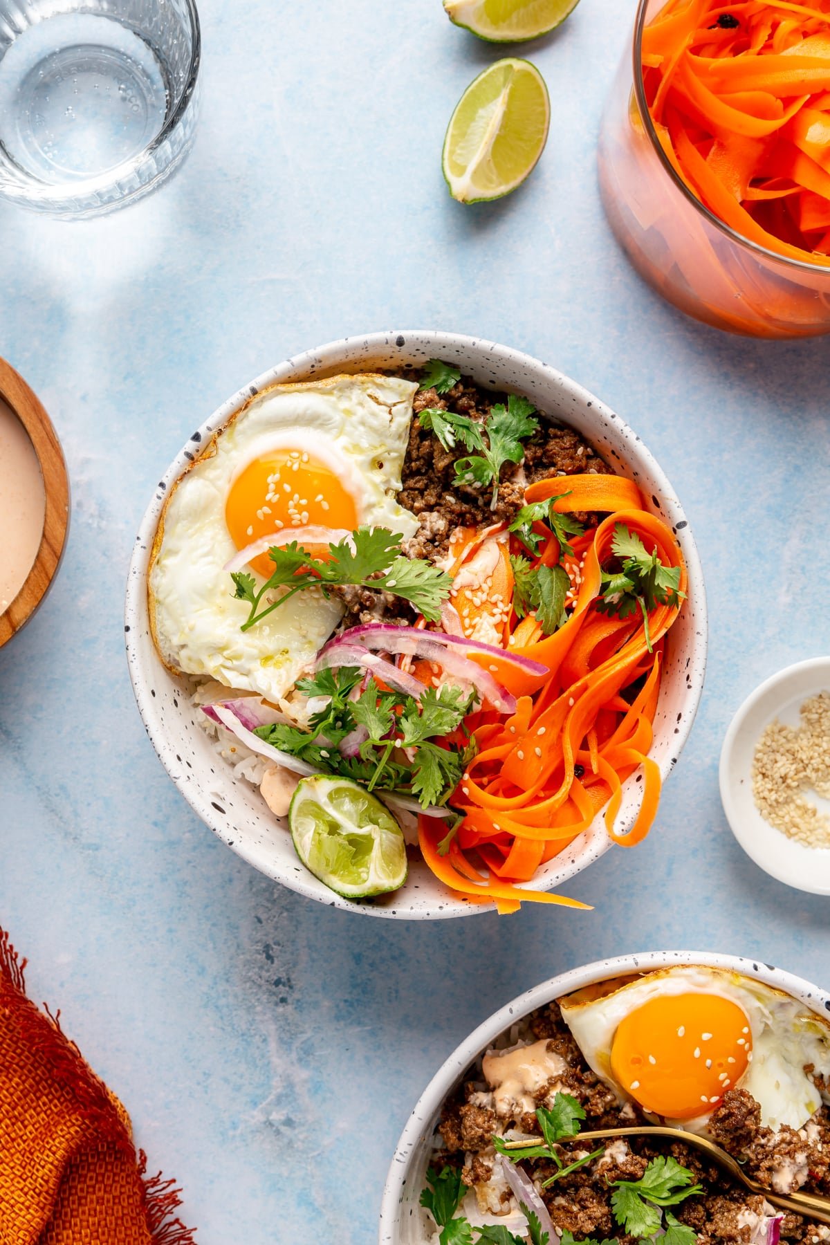 A Korean-inspired ground beef bowl complete with white rice, ground beef, a fried egg, pickled onions and carrots, cilantro, and sriracha mayonnaise.