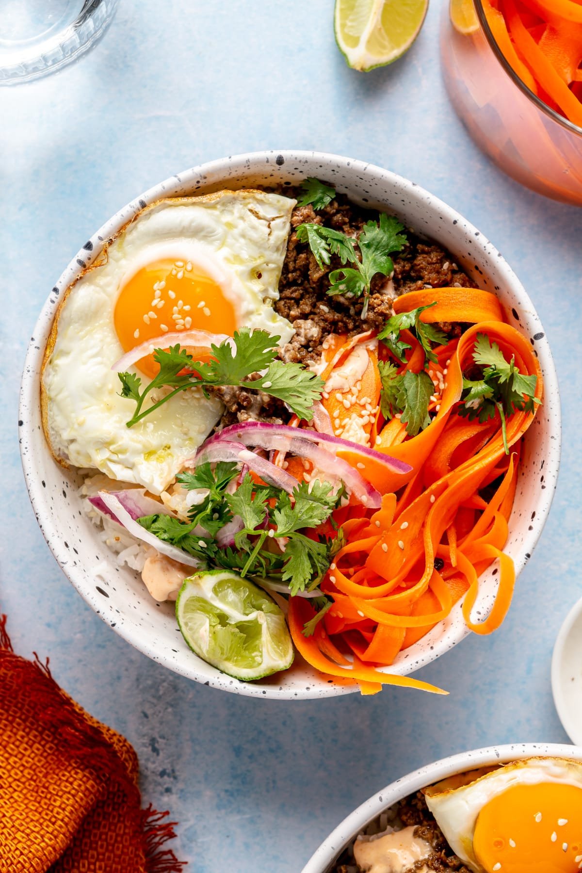 A Korean-inspired ground beef bowl complete with white rice, ground beef, a fried egg, pickled onions and carrots, cilantro, and sriracha mayonnaise.