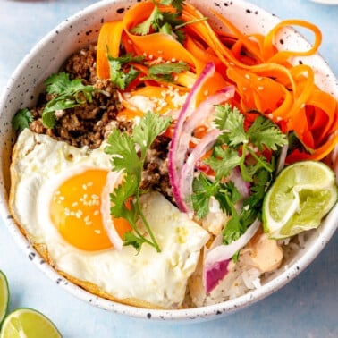 A Korean-inspired ground beef bowl complete with white rice, ground beef, a fried egg, pickled onions and carrots, cilantro, and sriracha mayonnaise.