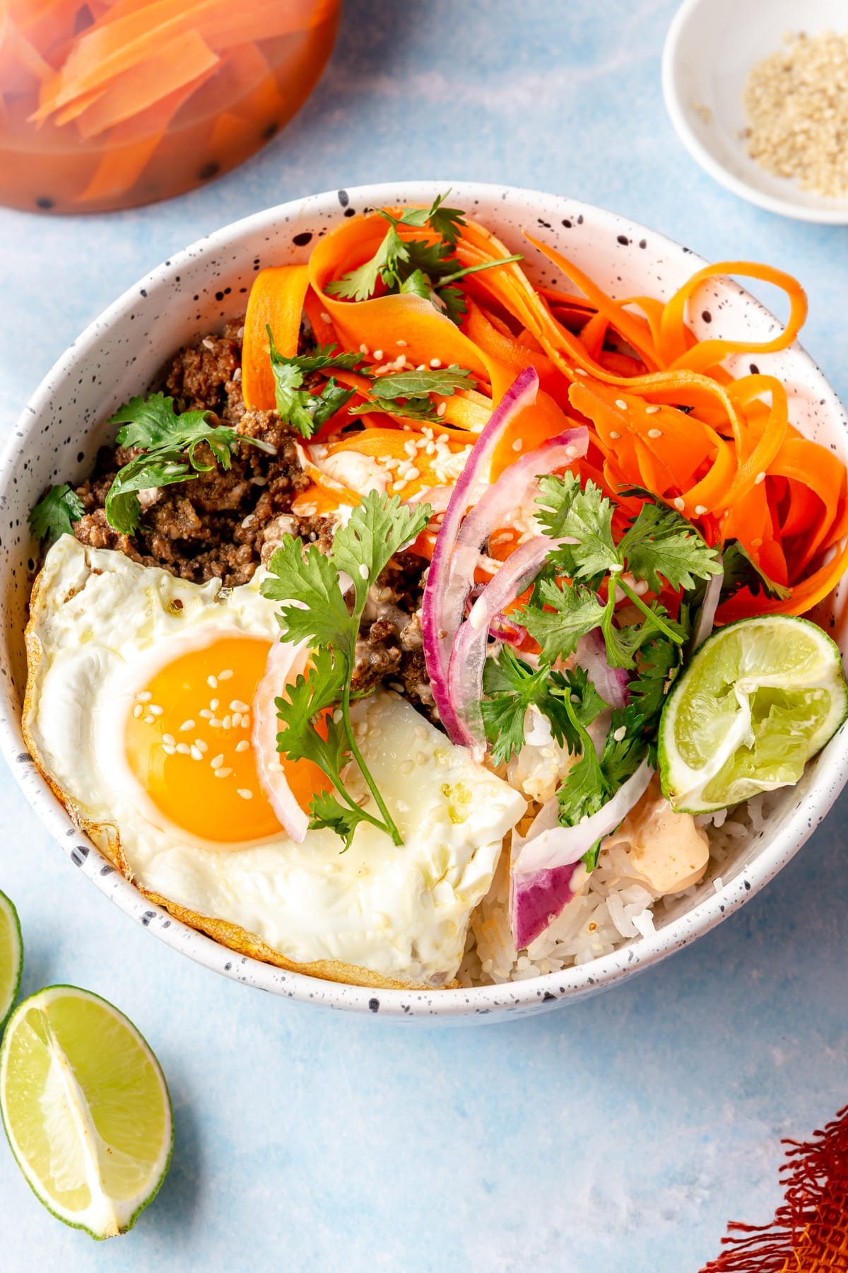 A Korean-inspired ground beef bowl complete with white rice, ground beef, a fried egg, pickled onions and carrots, cilantro, and sriracha mayonnaise.