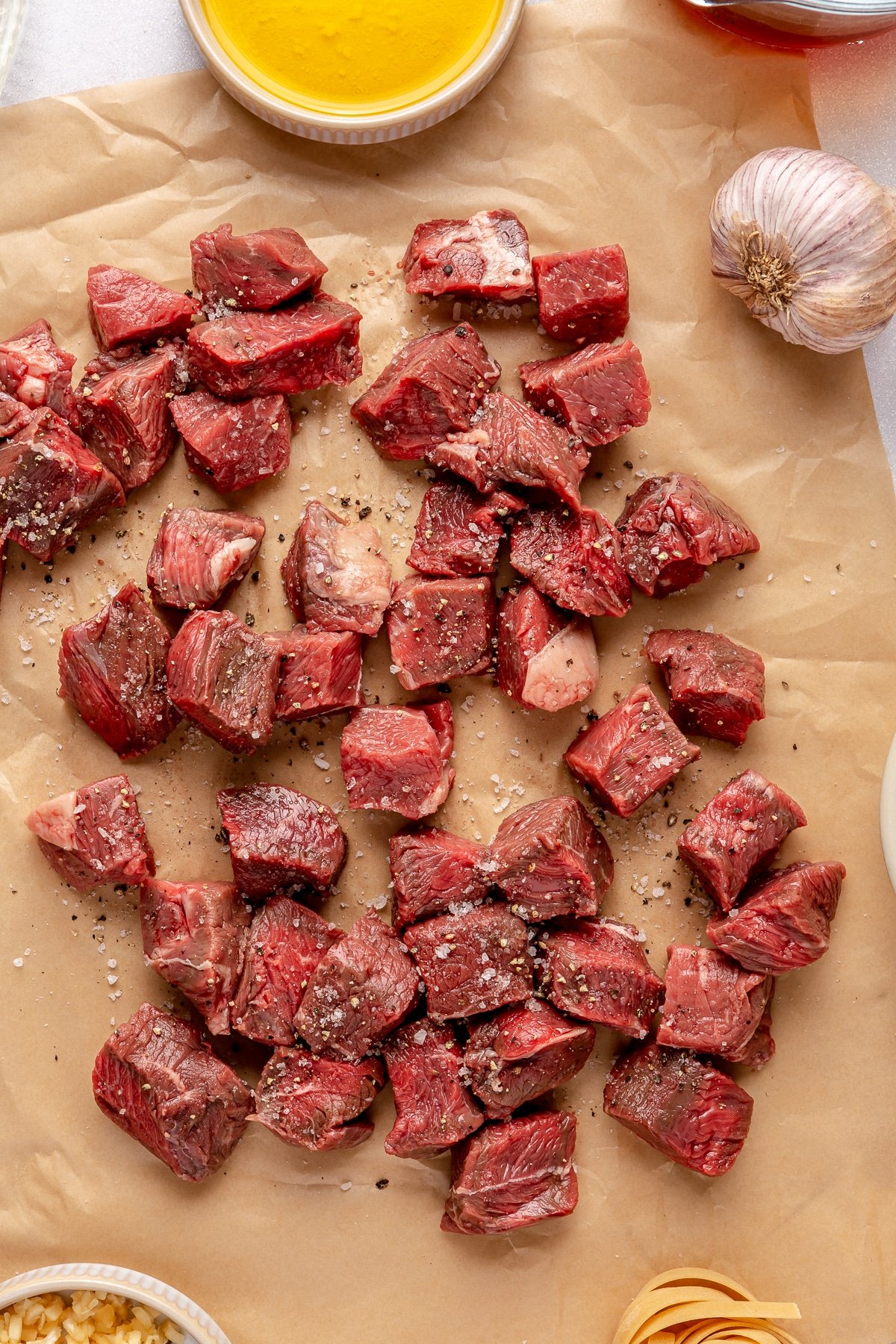 Steak tips tossed in salt and pepper on parchment paper.