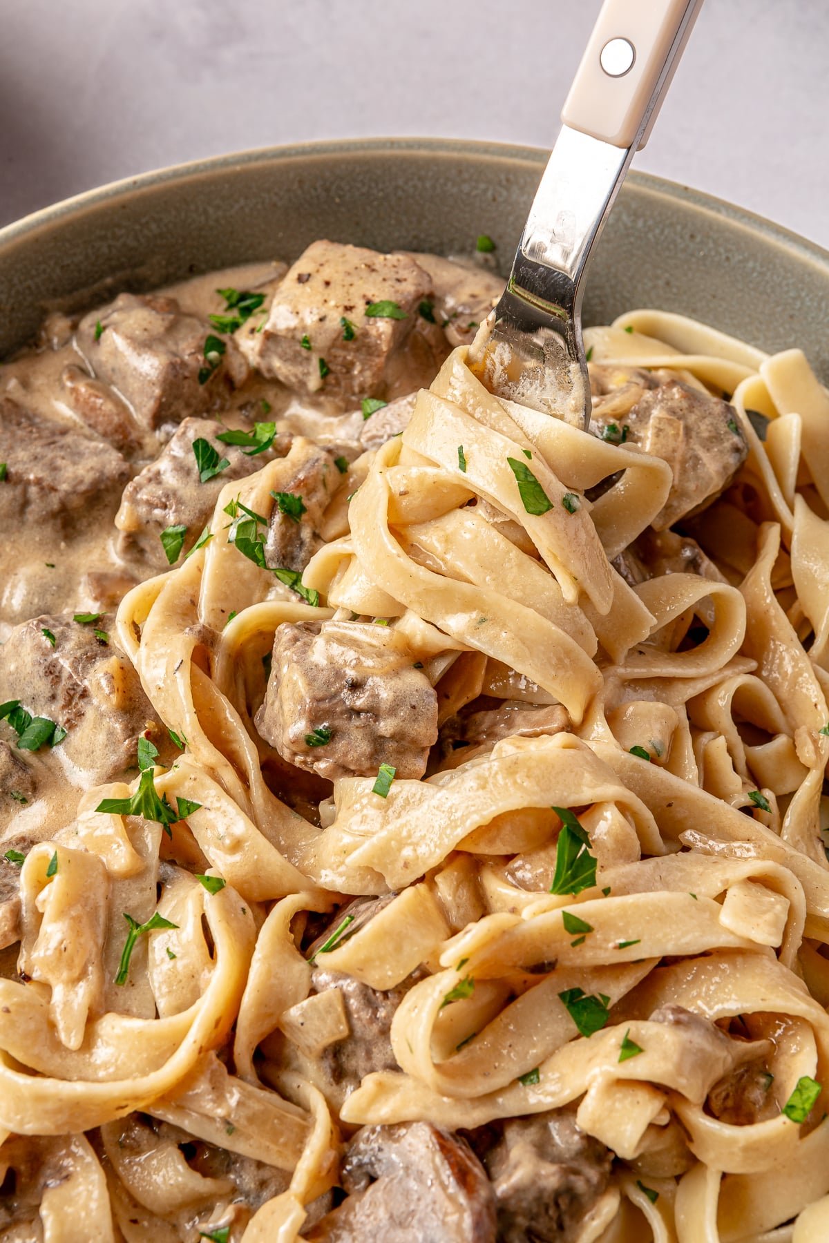 Someone using a fork to get a bite of beef stroganoff and noodles.