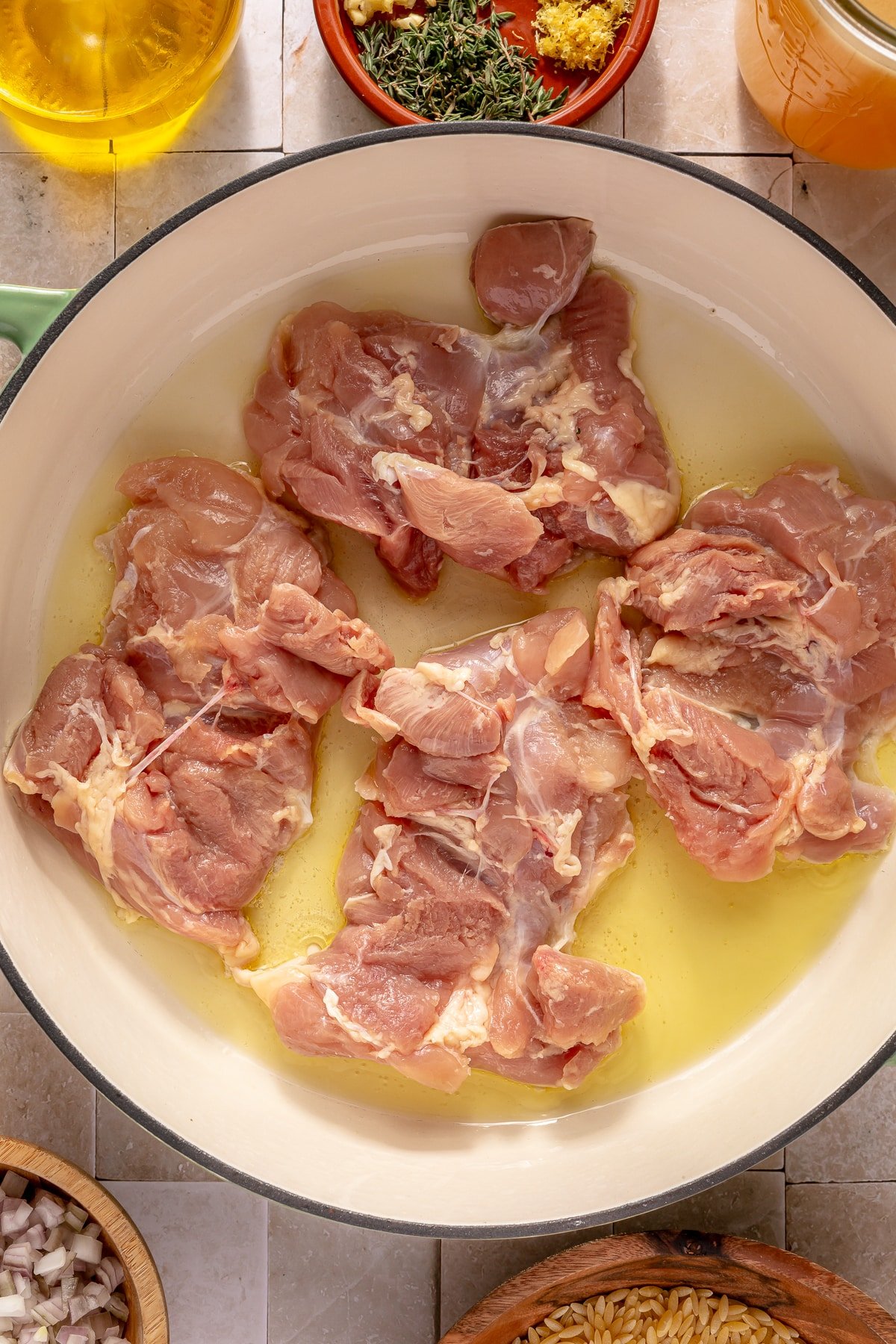 Chicken thighs searing in olive oil in an enameled cast iron pot.