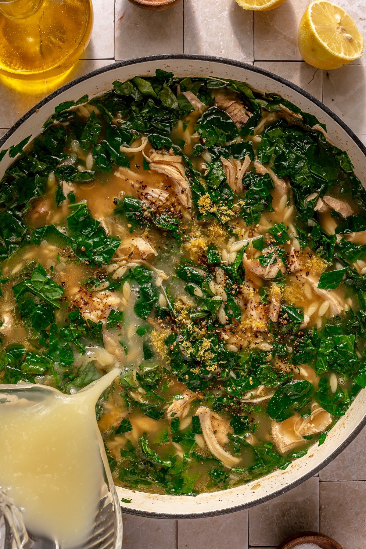 A person adding lemon juice into a pot of Lemon Chicken Orzo soup.