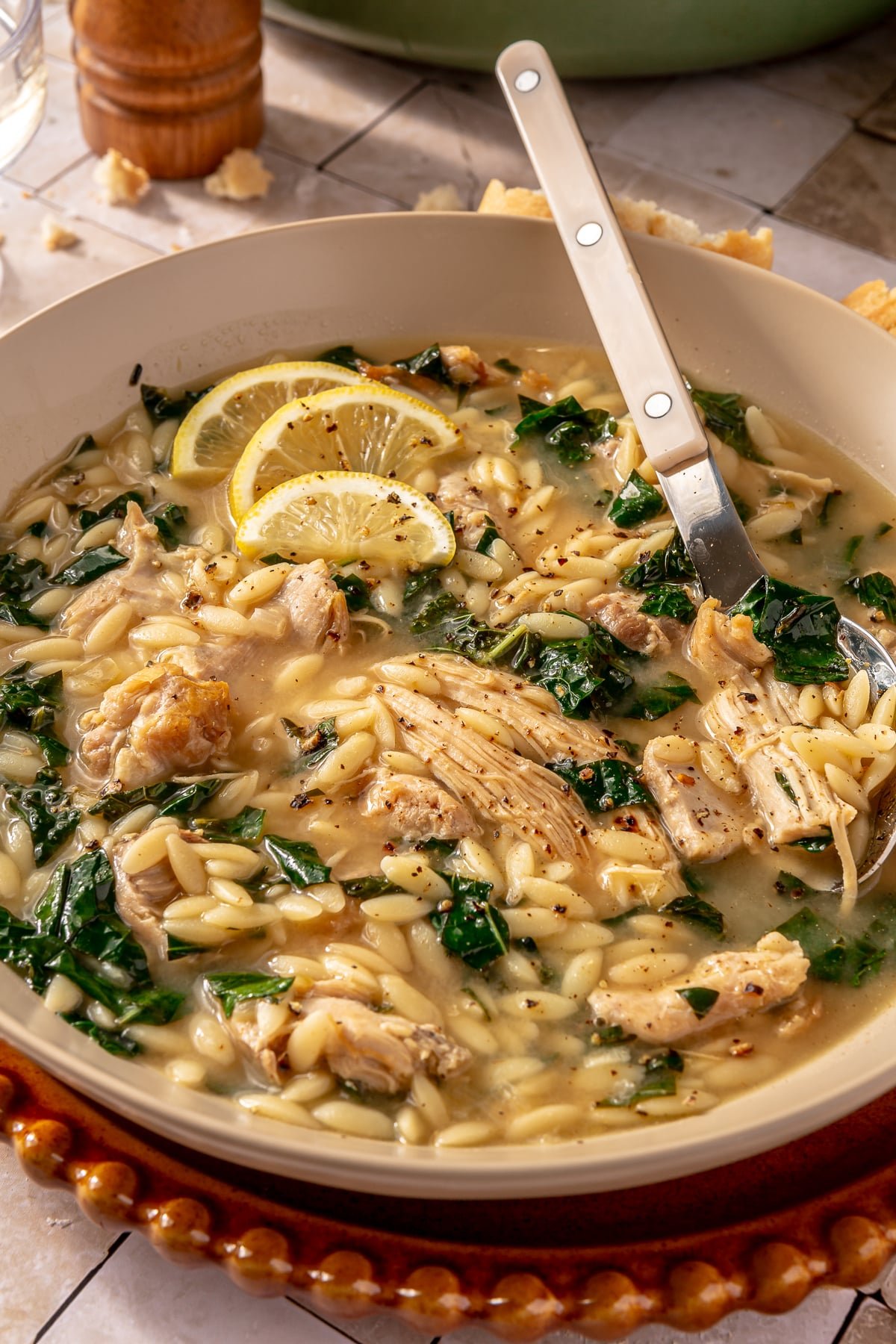 A bowl of lemon chicken orzo soup with a spoon in it.