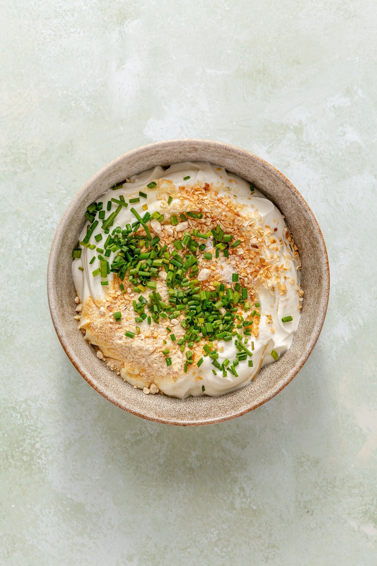 A bowl of Greek yogurt, sour cream, and all of the seasonings needed for homemade French onion dip.