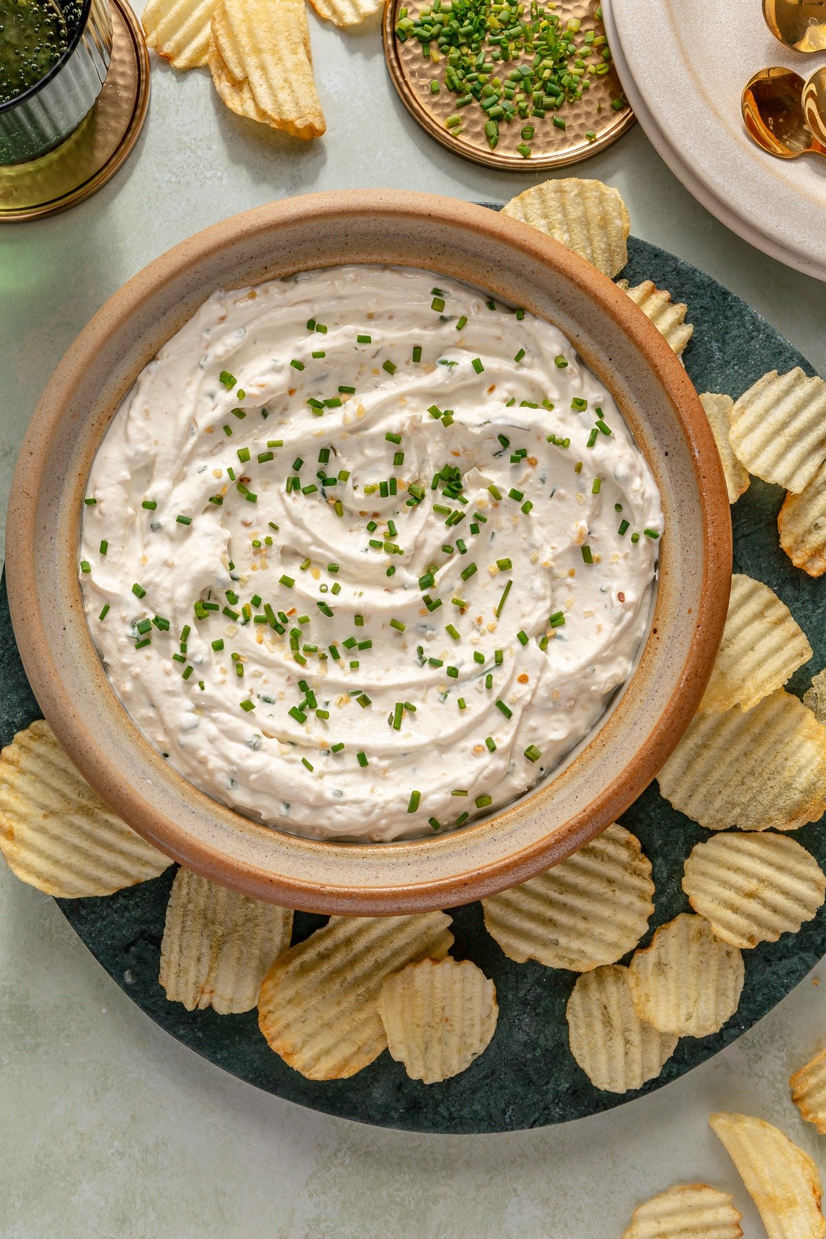 A large bowl of French onion dip garnished with fresh chives and surrounded by potato chips.