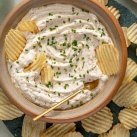 A large bowl of French onion dip garnished with fresh chives and surrounded by potato chips.