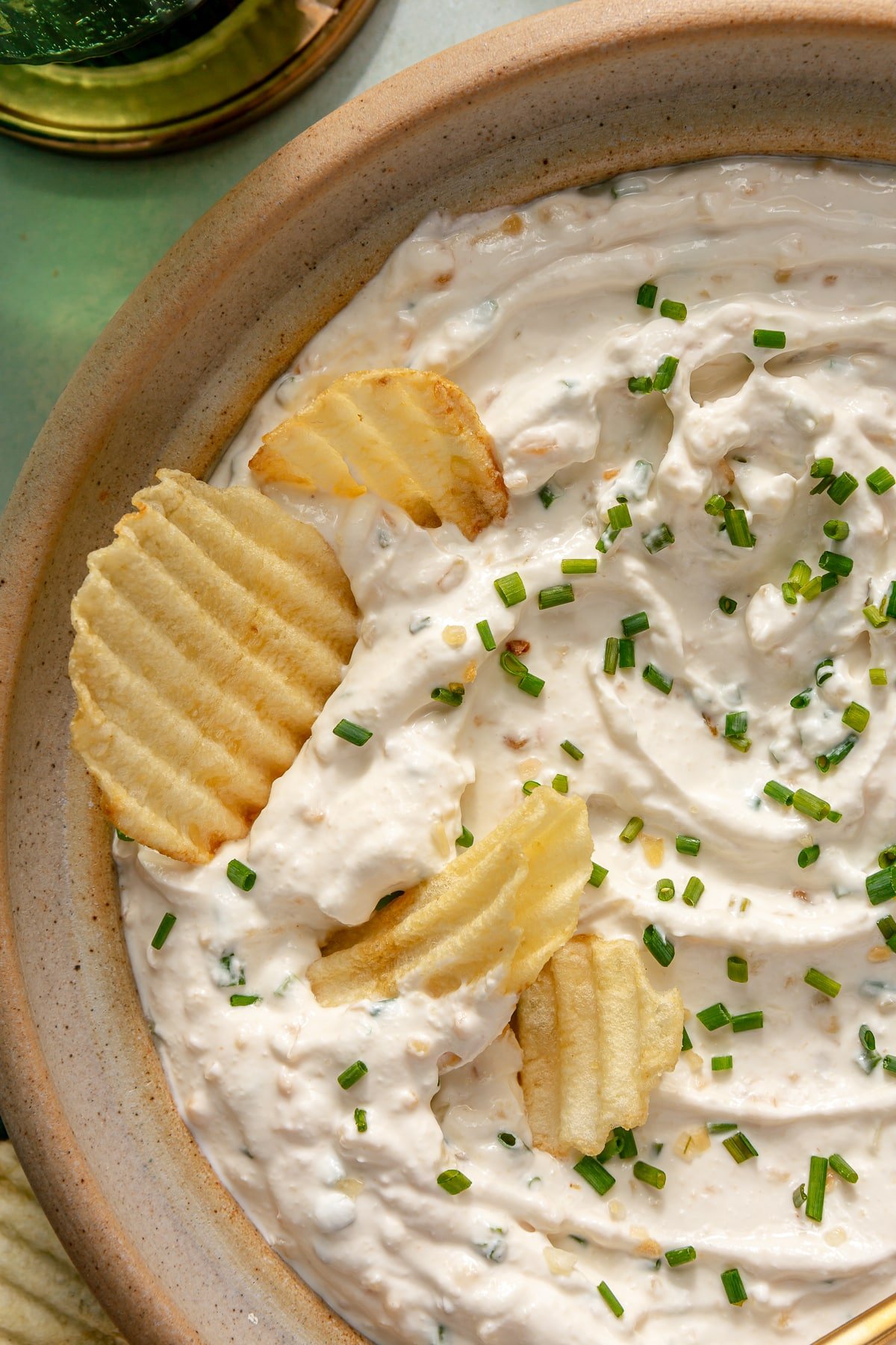 A bowl of homemade French Onion dip garnished with fresh chives and 4 potato chips sitting in the dip.