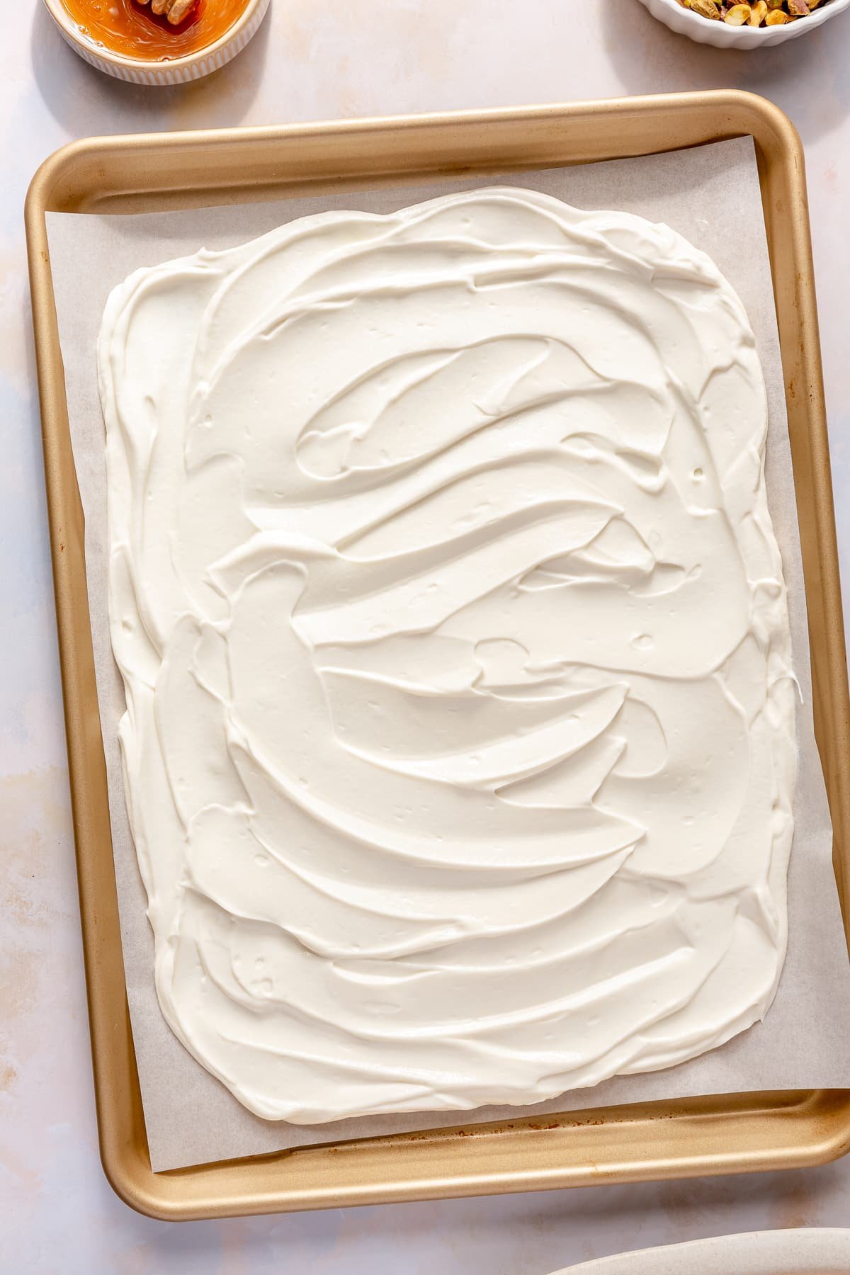 A parchment paper lined sheet pan with a honey yogurt mixture spread out evenly on it to make peaches and cream yogurt bark.