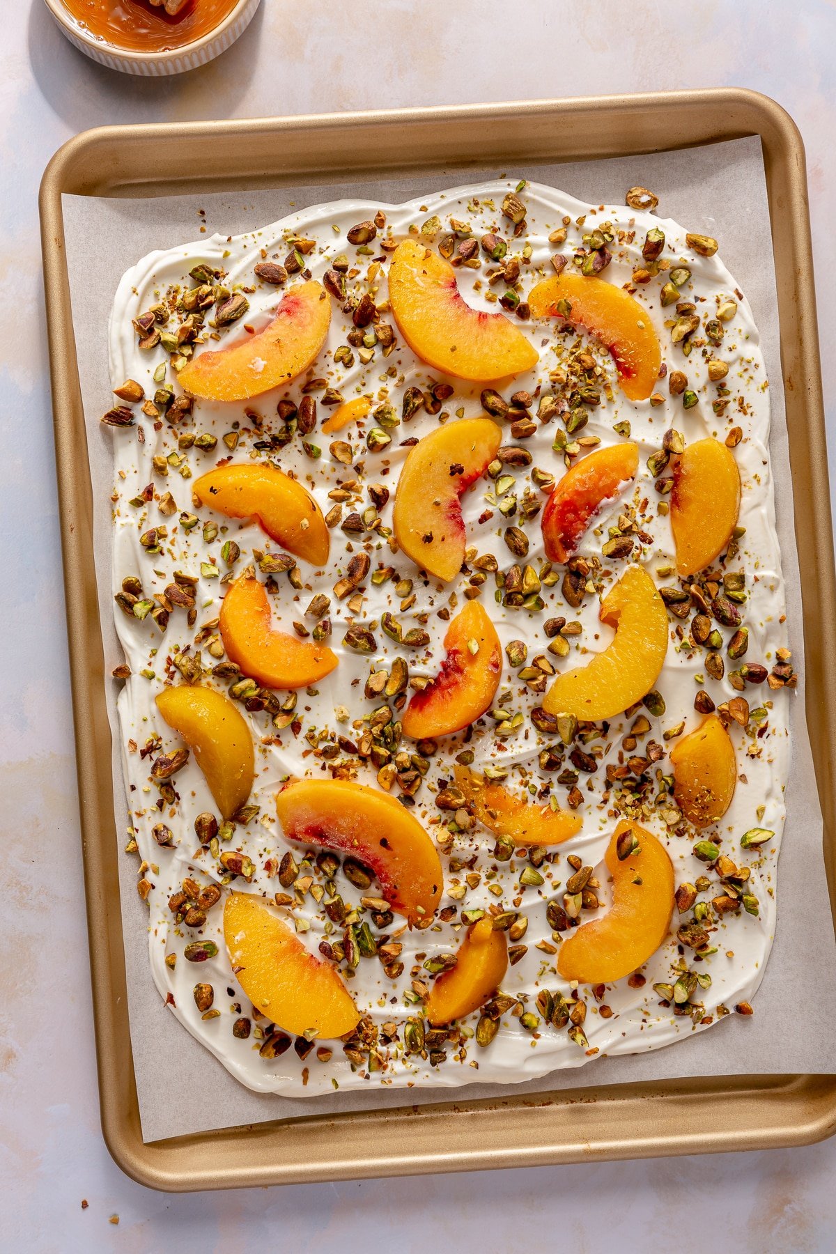 Peaches and cream yogurt bark on a parchment paper lined sheet pan before freezing.