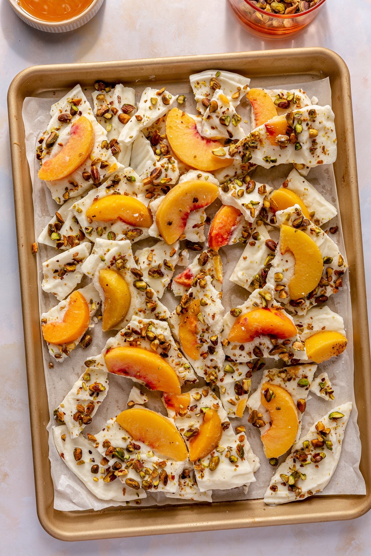 Peaches and cream frozen yogurt bark sitting in a parchment paper lined baking sheet.