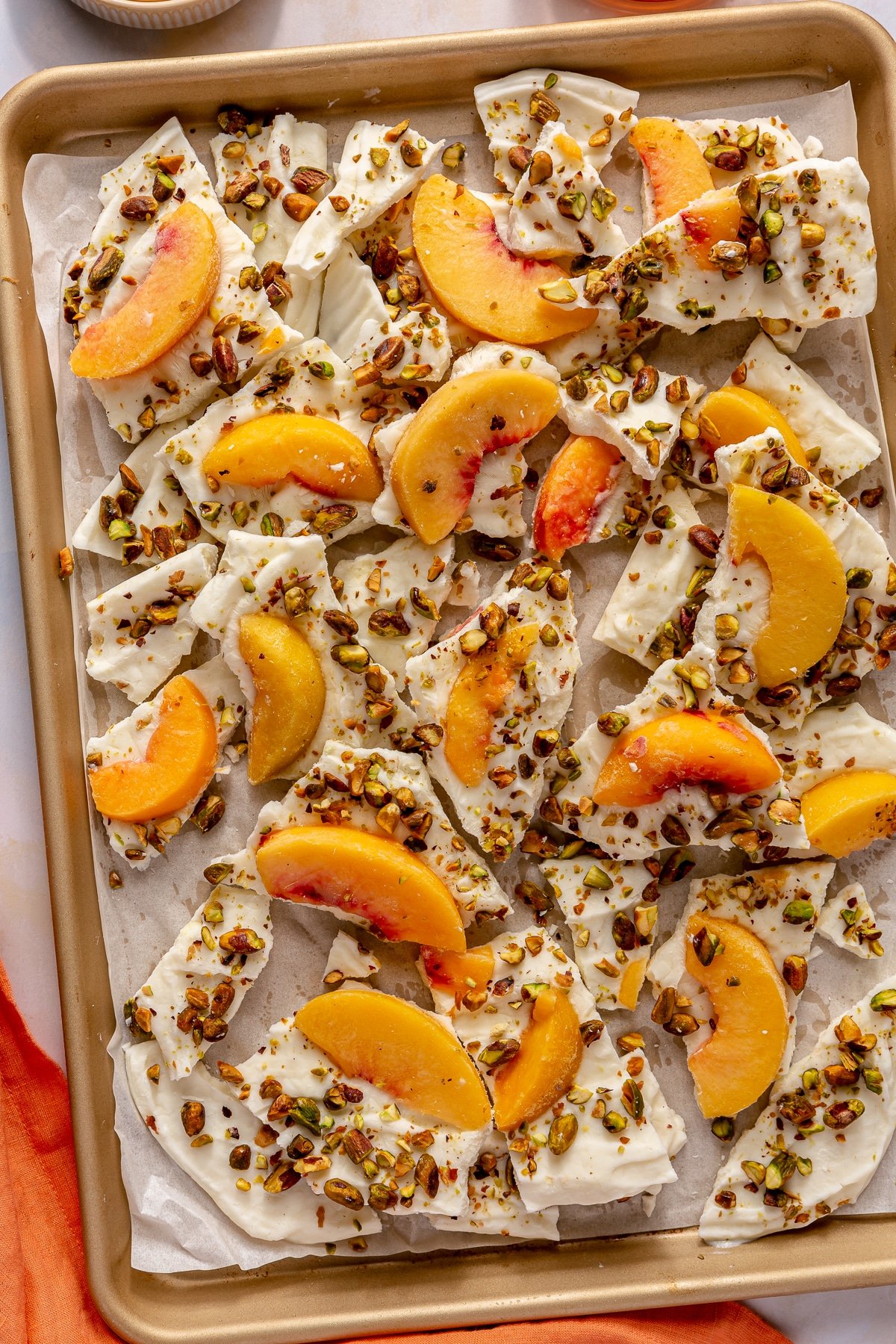 Peaches and cream frozen yogurt bark sitting in a parchment paper lined baking sheet.
