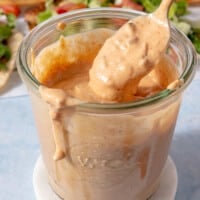 A jar of burger sauce with someone using a spoon to scoop some out of the jar.