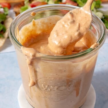 A jar of burger sauce with someone using a spoon to scoop some out of the jar.