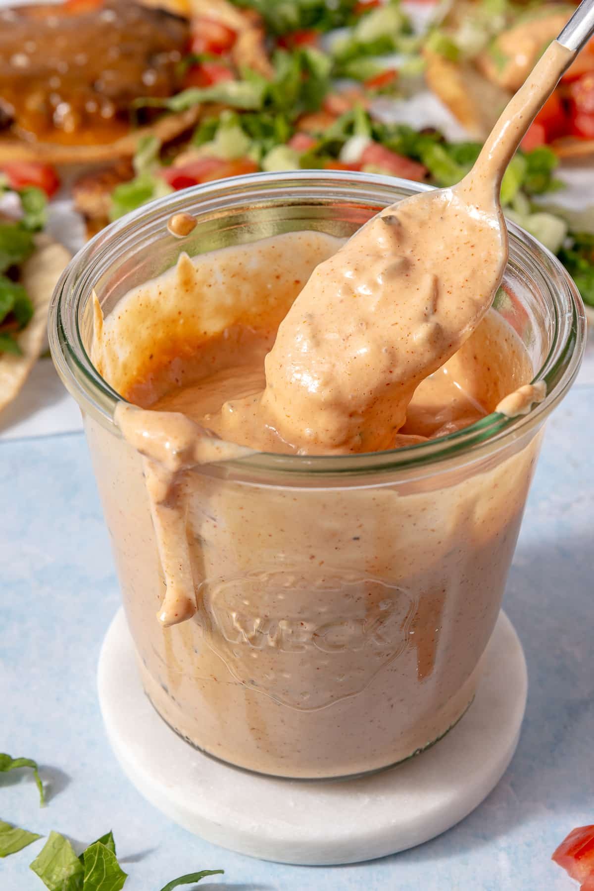 A jar of burger sauce with someone using a spoon to scoop some out of the jar.