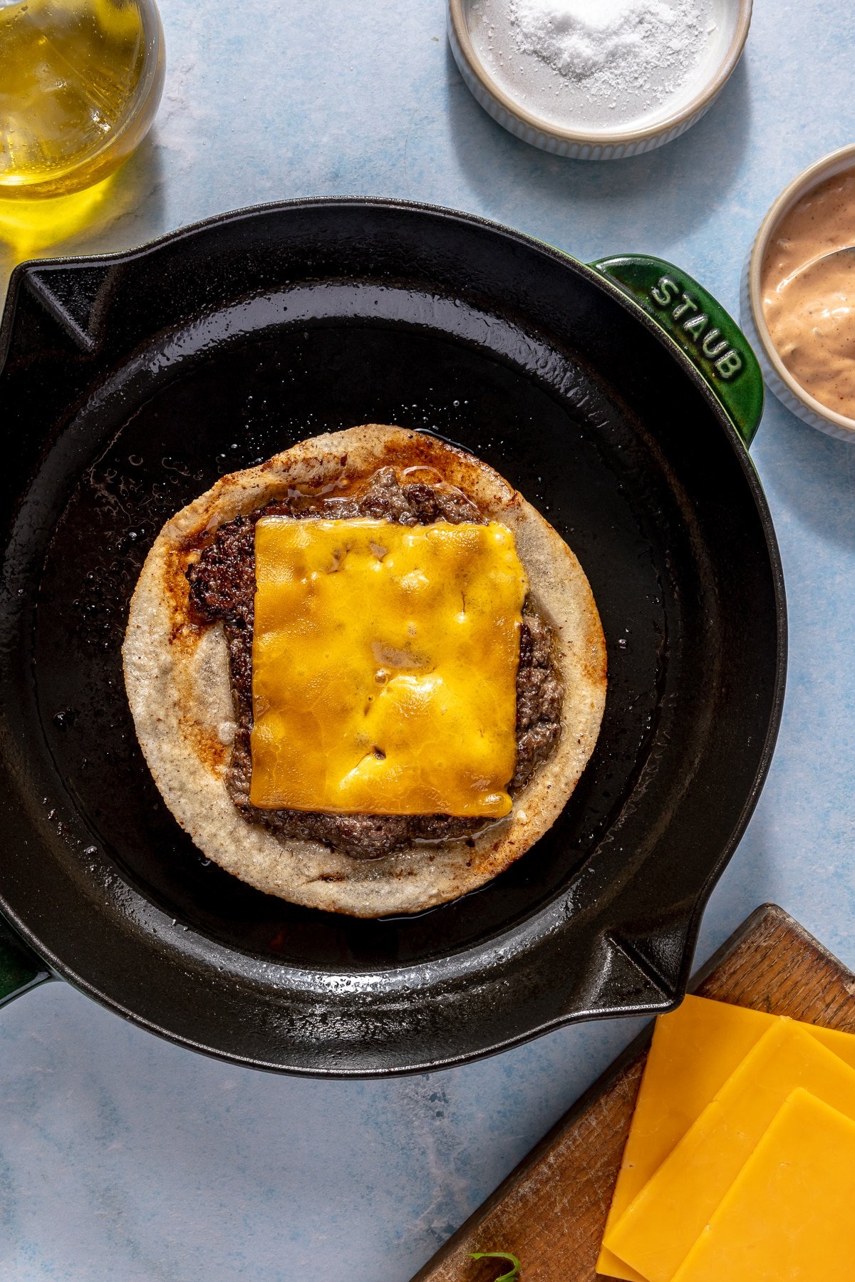 A smash burger taco cooking on a cast iron skillet.