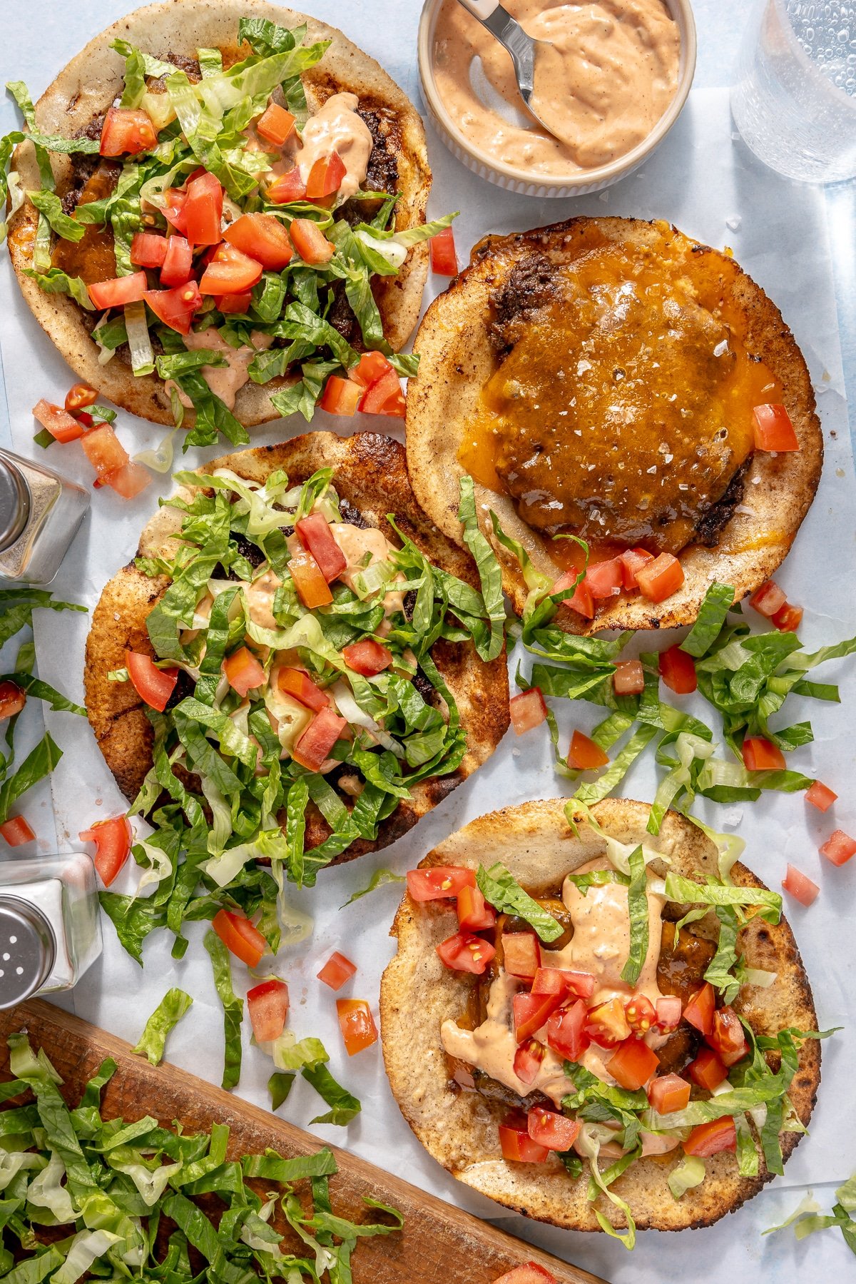 A smash burger taco garnished with burger sauce, diced tomatoes, and shredded lettuce.
