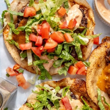 A smash burger taco garnished with burger sauce, diced tomatoes, and shredded lettuce.