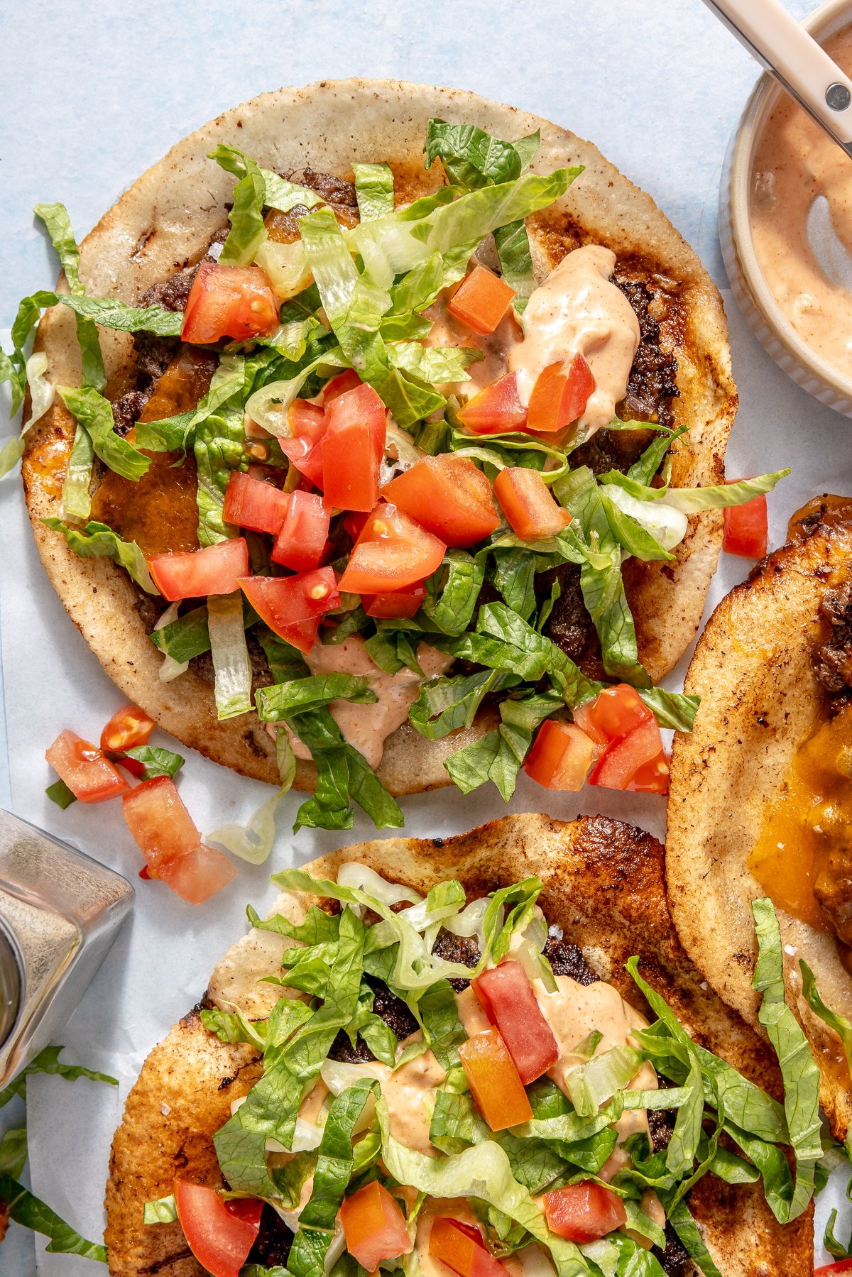 A smash burger taco garnished with burger sauce, diced tomatoes, and shredded lettuce.
