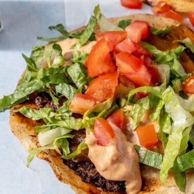 A smash burger taco garnished with burger sauce, diced tomatoes, and shredded lettuce.