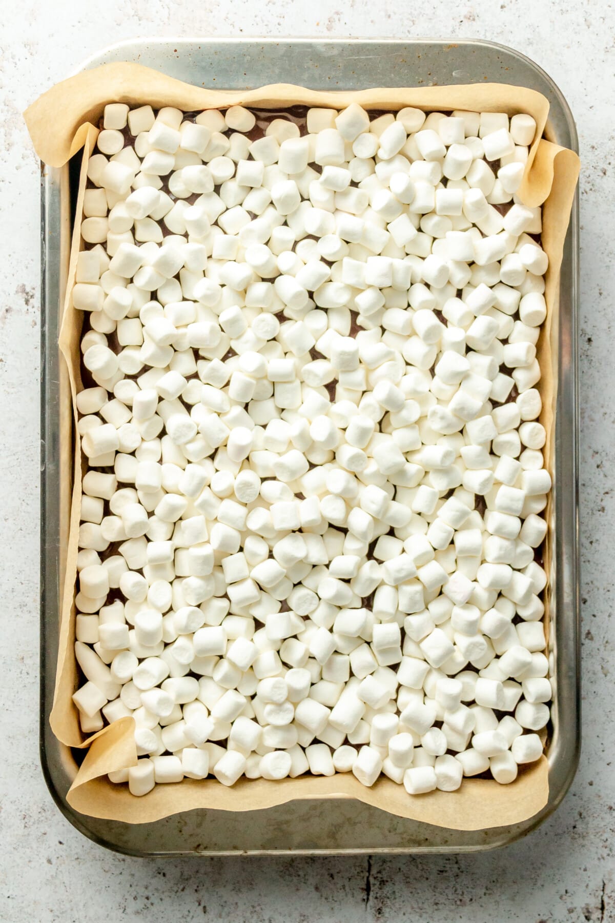 Mini marshmallows sit on a lined rimmed tray on a light grey surface.