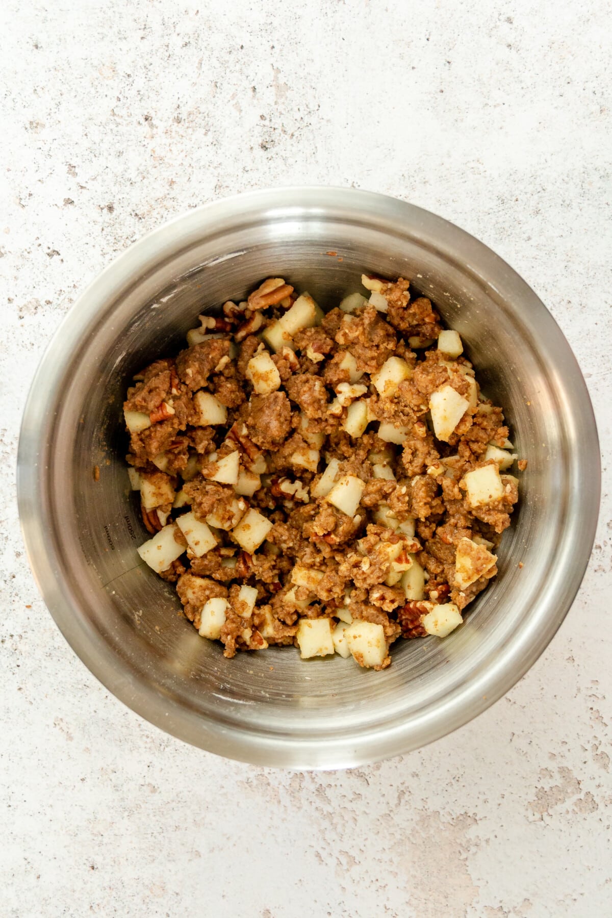 An apple crumb mixture sits in a stainless steel bowl on a light grey surface.