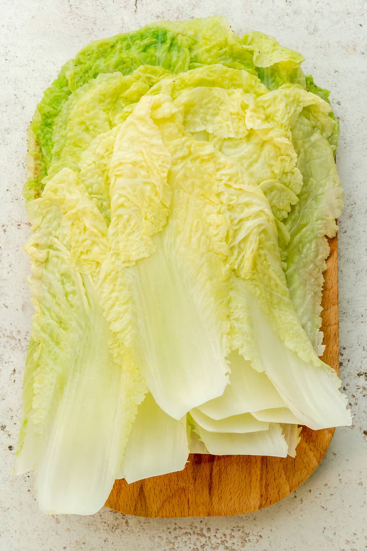 Cooked napa cabbage leaves sit on a wooden board on a light gray surface.