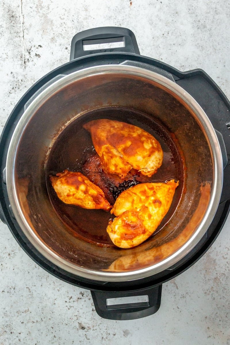 Cooked chicken breasts, surrounded in a dark brown sauce, sit in the bottom of a pressure cooker.