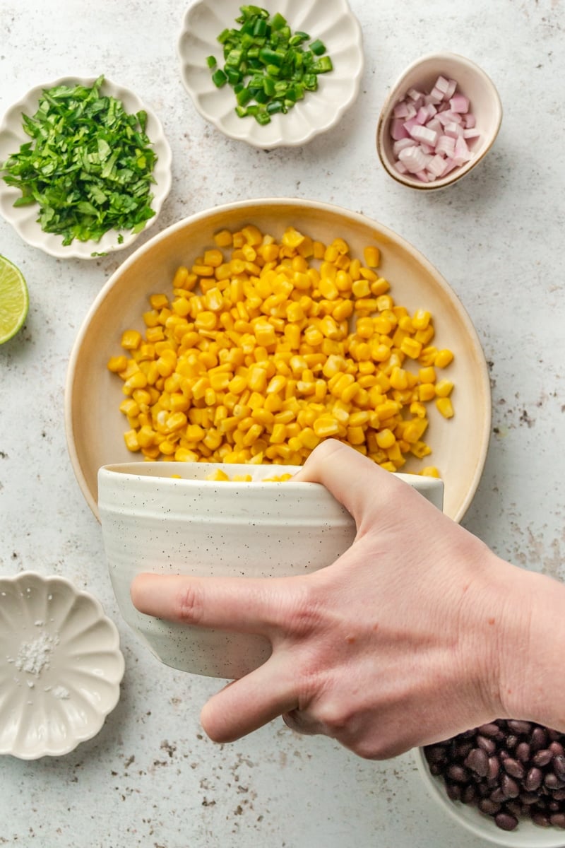 A bowl of corn is shown being poured into a larger mixing bowl.