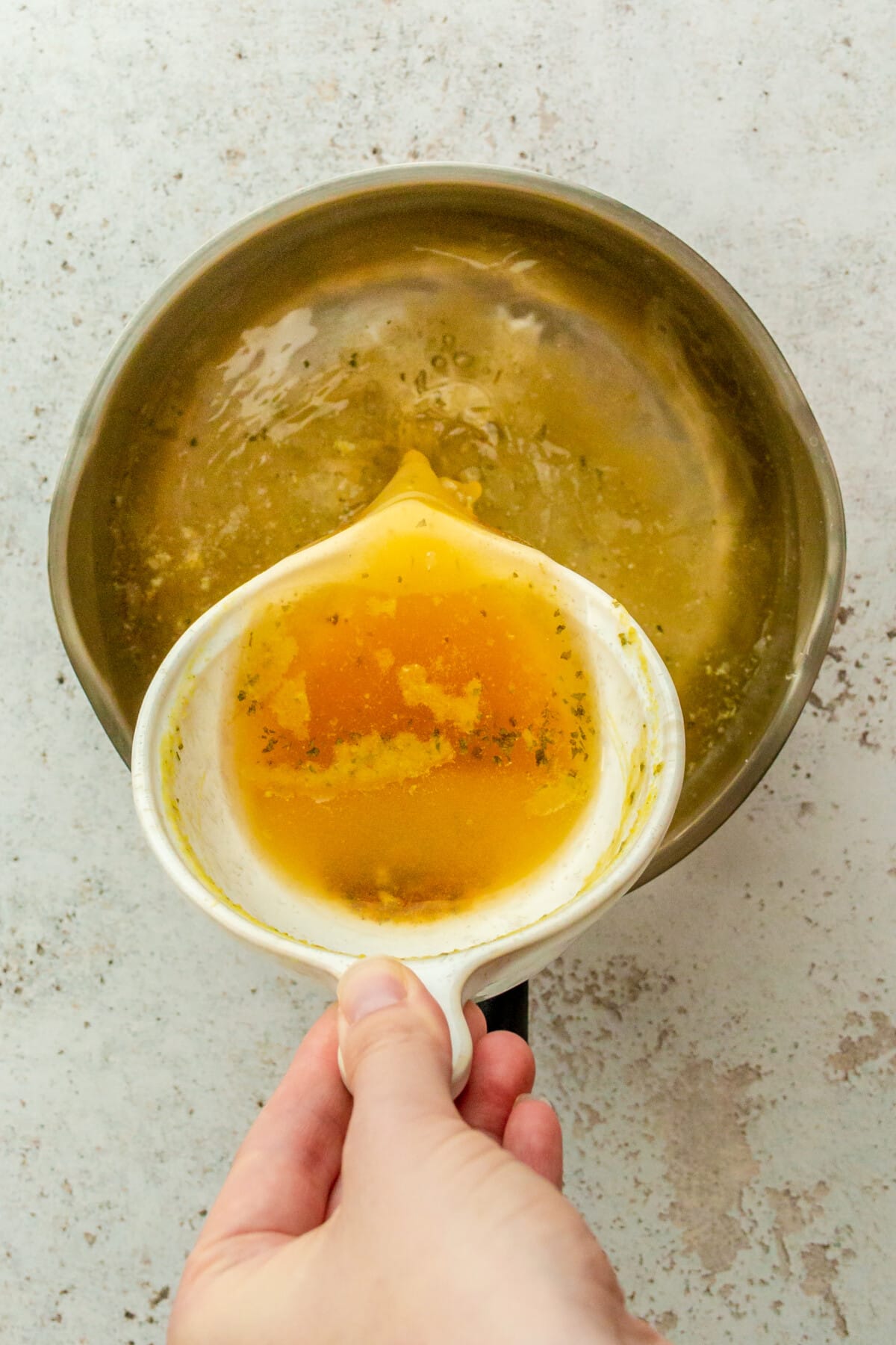 Broth is poured in a stainless steel saucepan on a light grey surface.