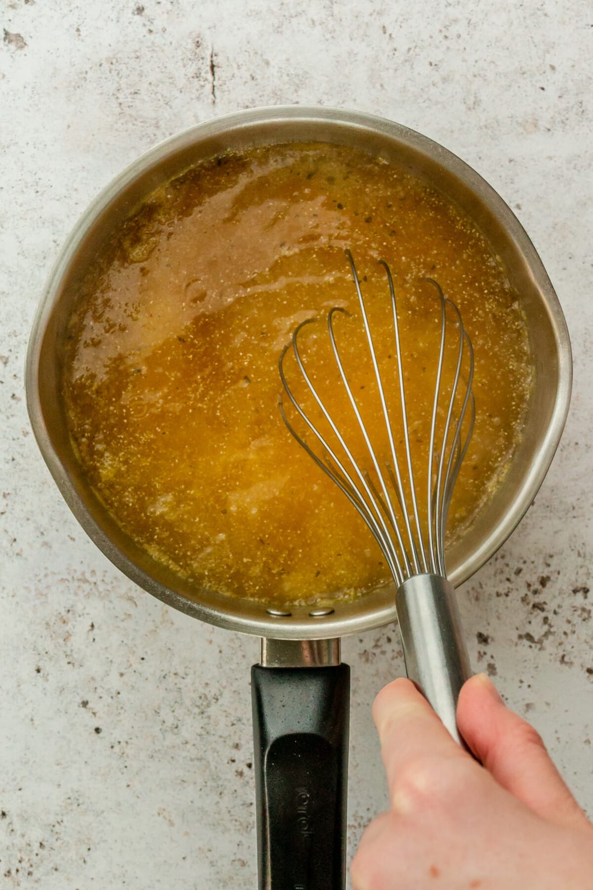 Polenta is whisked in broth in a steel saucepan on a light grey surface.