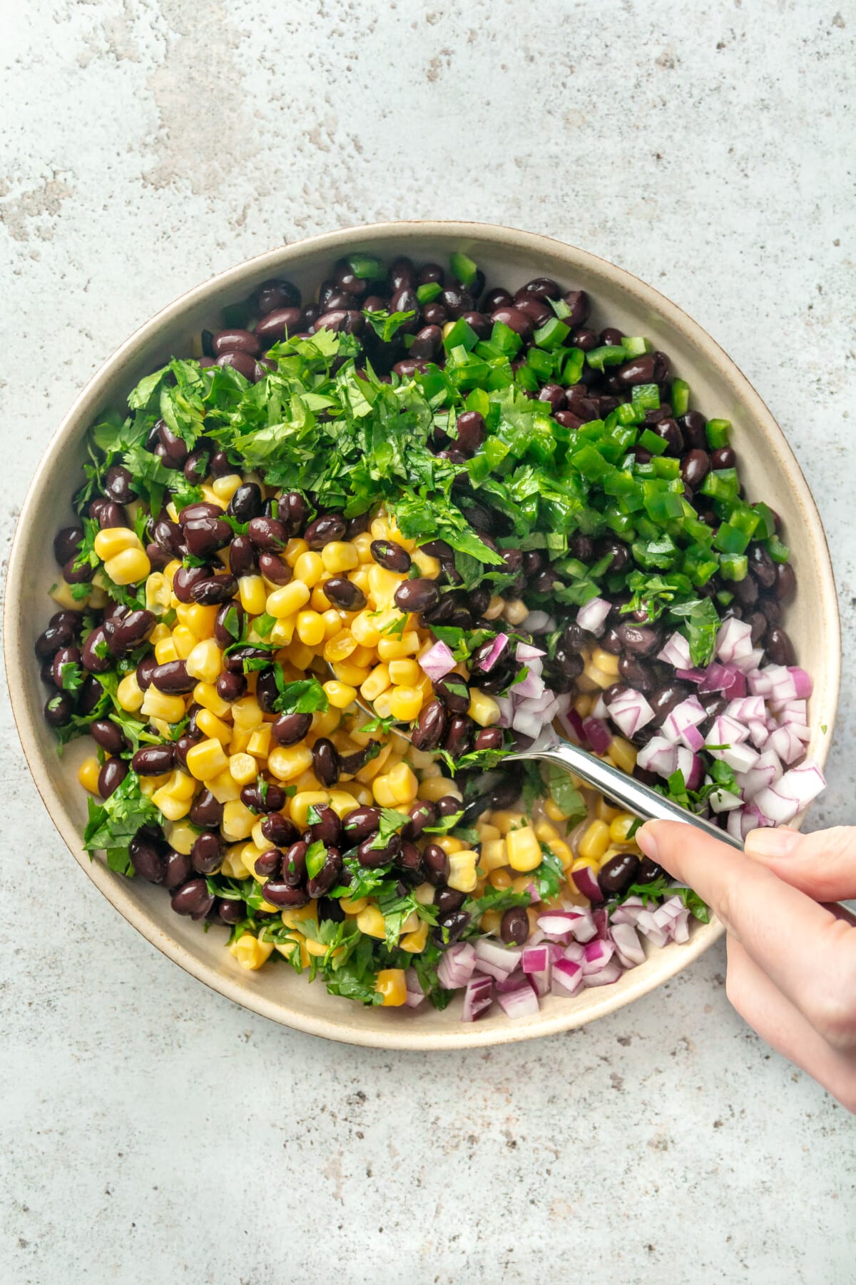 A person using a spoon to mix together ingredients for a black bean and corn salsa.