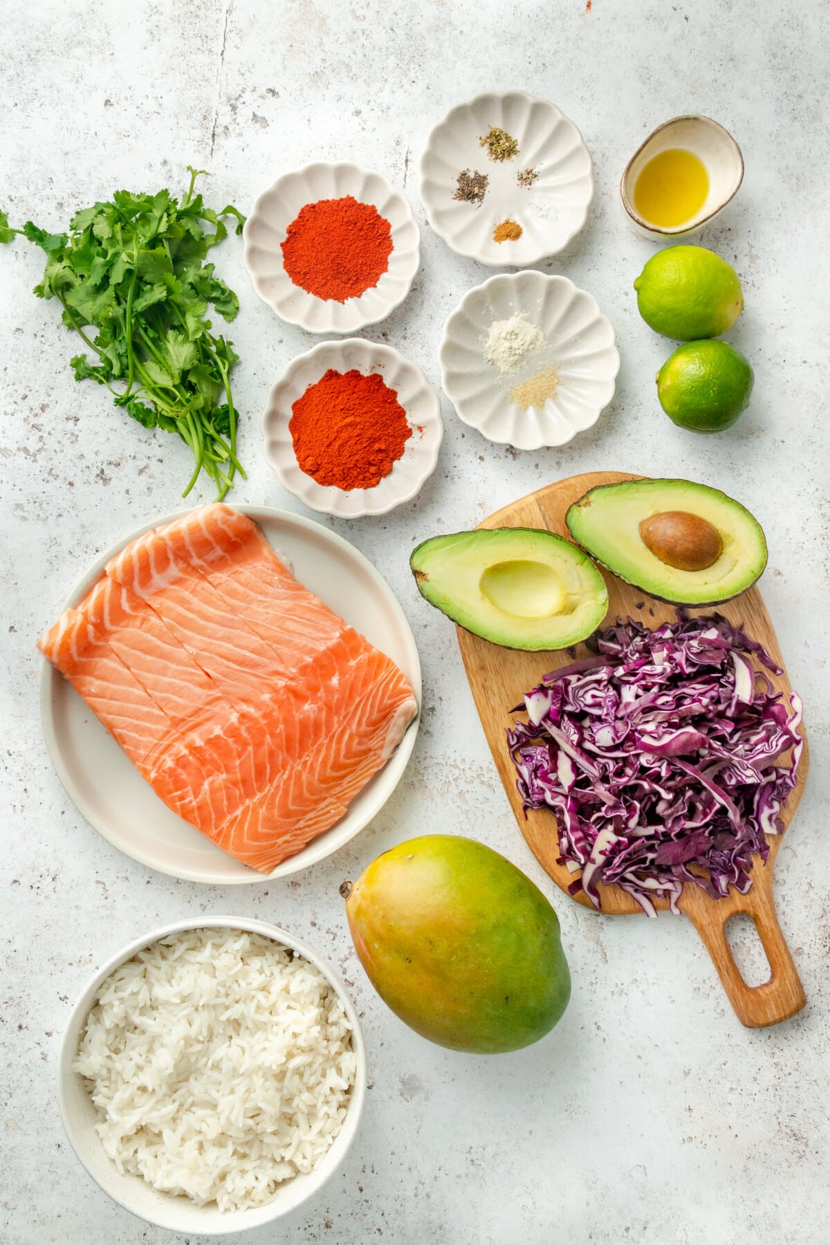 Ingredients for blackened salmon bowls with coconut rice sit in a variety of bowls on a light grey colored surface.
