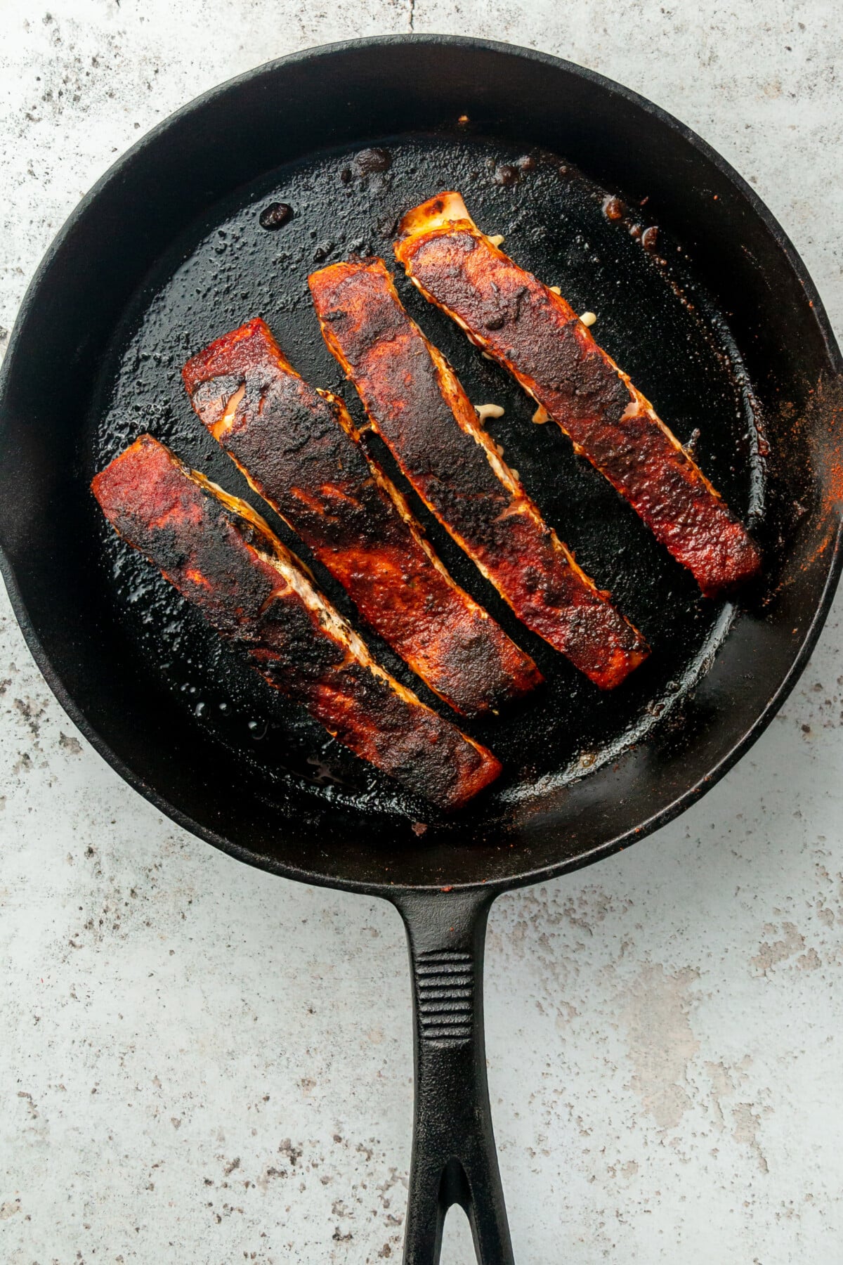 Blackened salmon sits in a cast iron skillet on a light grey colored surface.